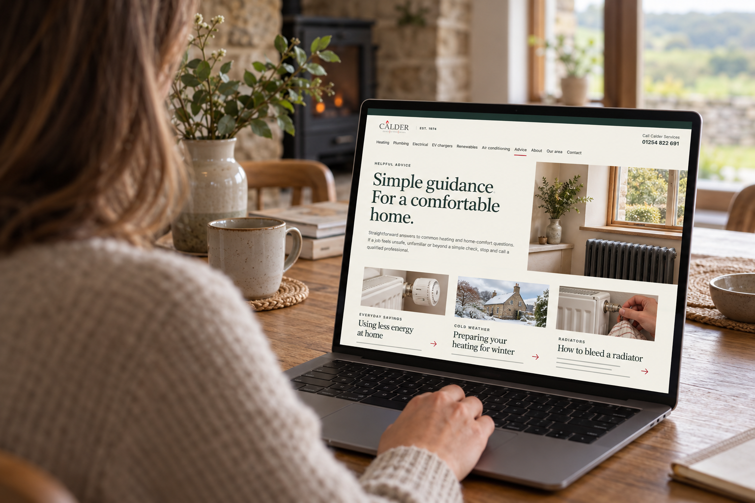 A homeowner viewing the Calder Services advice page on a laptop in a warm stone home